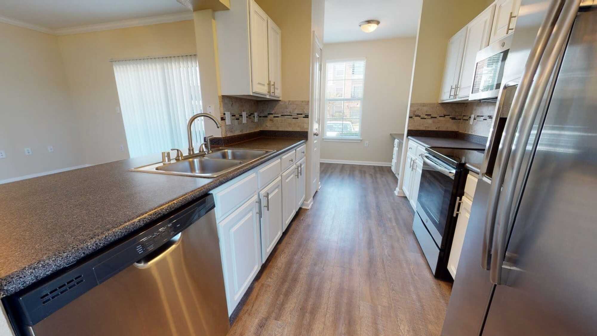 Modern kitchen with stainless steel appliances, white cabinets, wood flooring, and large window providing natural light.