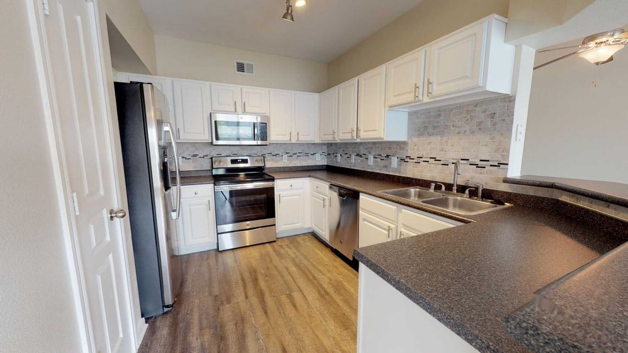 Modern kitchen with white cabinets, stainless steel appliances, tile backsplash, and wood-style flooring.