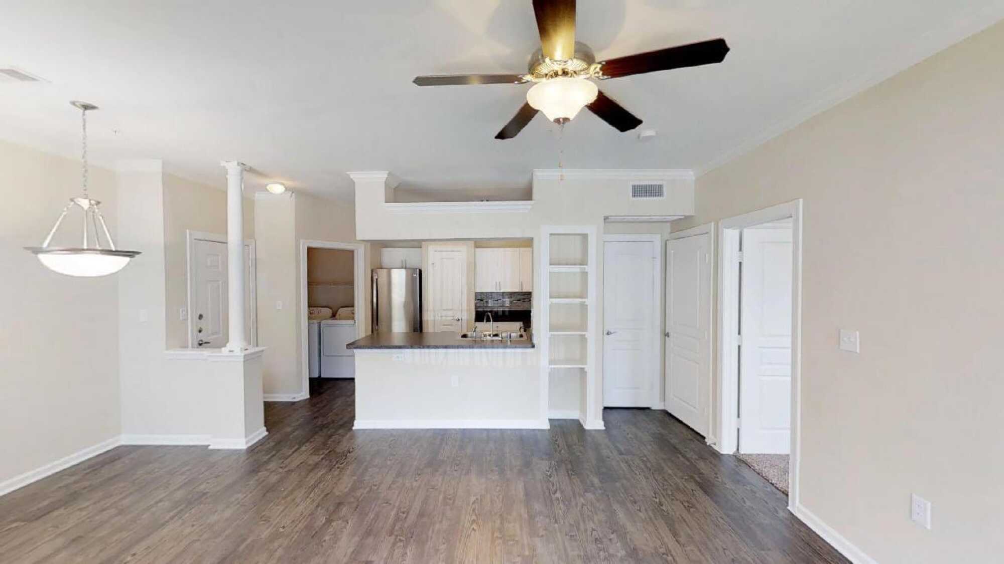 Modern kitchen with stainless steel appliances, open shelves, white cabinets, ceiling fan, and wood flooring. Laundry area visible on the left.