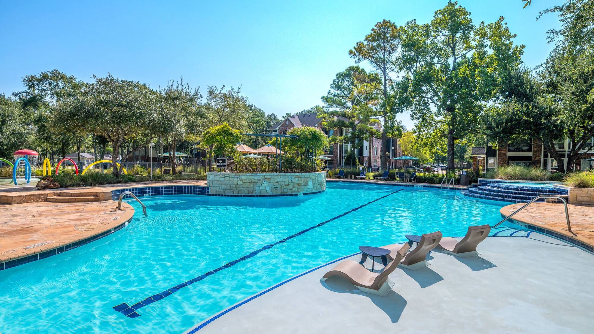 Coles Crossing sparkling pool with stone water feature and sundeck loungers in Cypress, Texas apartments.