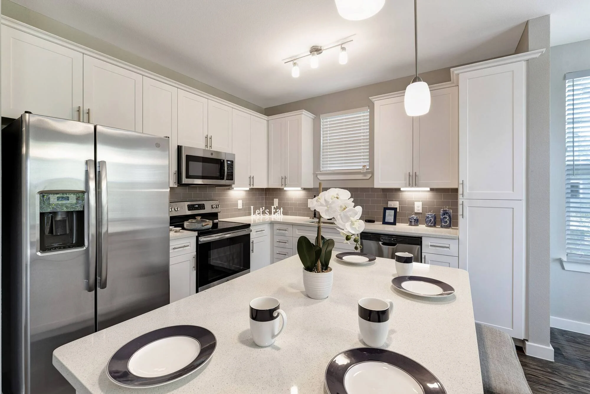 Gourmet kitchen with white shaker cabinets, quartz island with place settings, and stainless steel appliances at Coles Crossing in Cypress, Texas