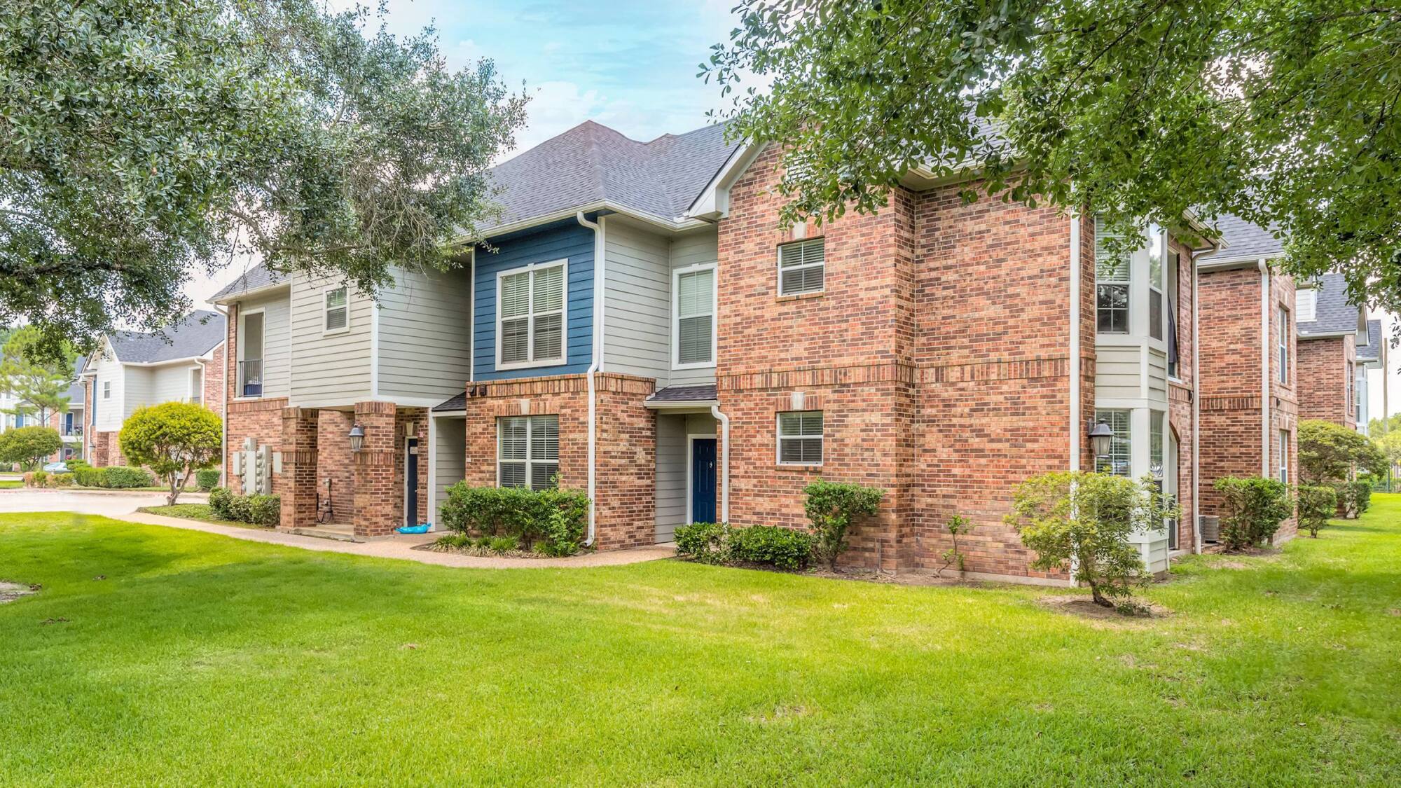 Coles Crossing apartment building exterior with brick and blue siding on manicured grounds in Cypress, Texas.